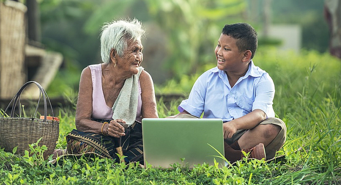 Бабушка смотрит на мальчика, который показывает ей ноутбук.