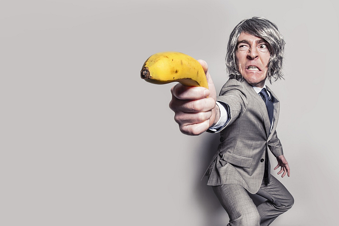 Испуганный мужчина в сером костюме держит банан как пистолет