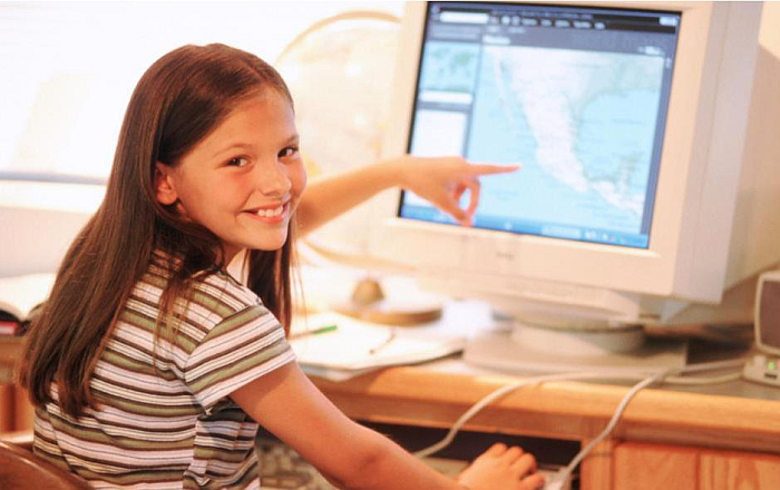 Девочка сидит за компьютером и улыбается, показывает пальцем на карту Центральной Америки